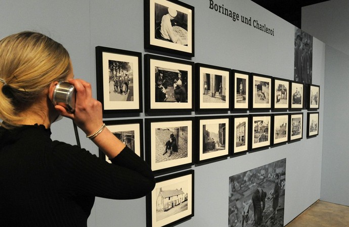 Eine Frau an einer Hörstation vor einer Wand mit Fotografien.