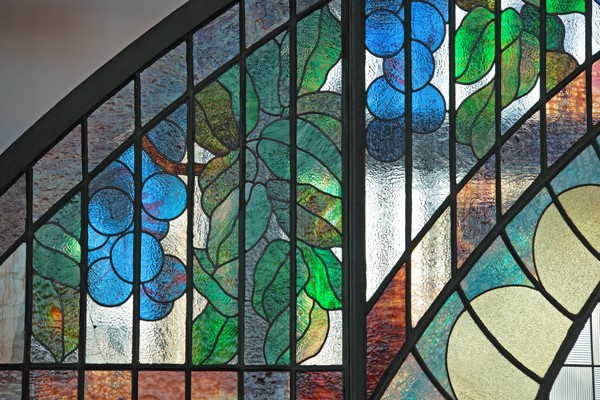 Windfang des Jugendstilportals mit farbigen Glasdetails in floralen Formen.