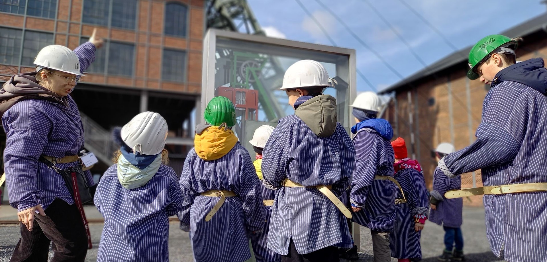 Kinder mit Grubenhelmen ind Grubenhemden vor dem Fördergerüst