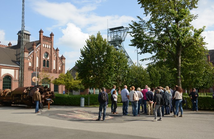 Besuchergruppe im Ehrenhof der Zeche Zollern; im Hintergrund Fördergerüst