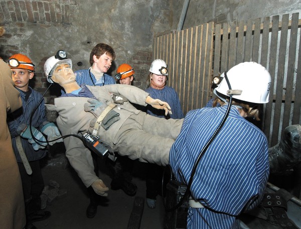 Kinder in Bergmannskleidung tragen eine lebensgroße Puppe, die einen verunglückten Bergmann darstellt, davon.