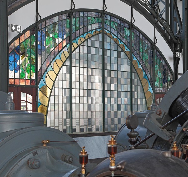 Windfang des Maschinenhallen-Portals mit farbiger Verglasung; vom Innern der Halle aus gesehen. Im Vordergrund Details von Maschinen.